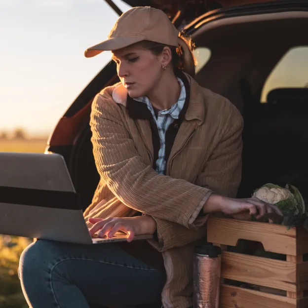 Woman on tailgate with laptop and produce