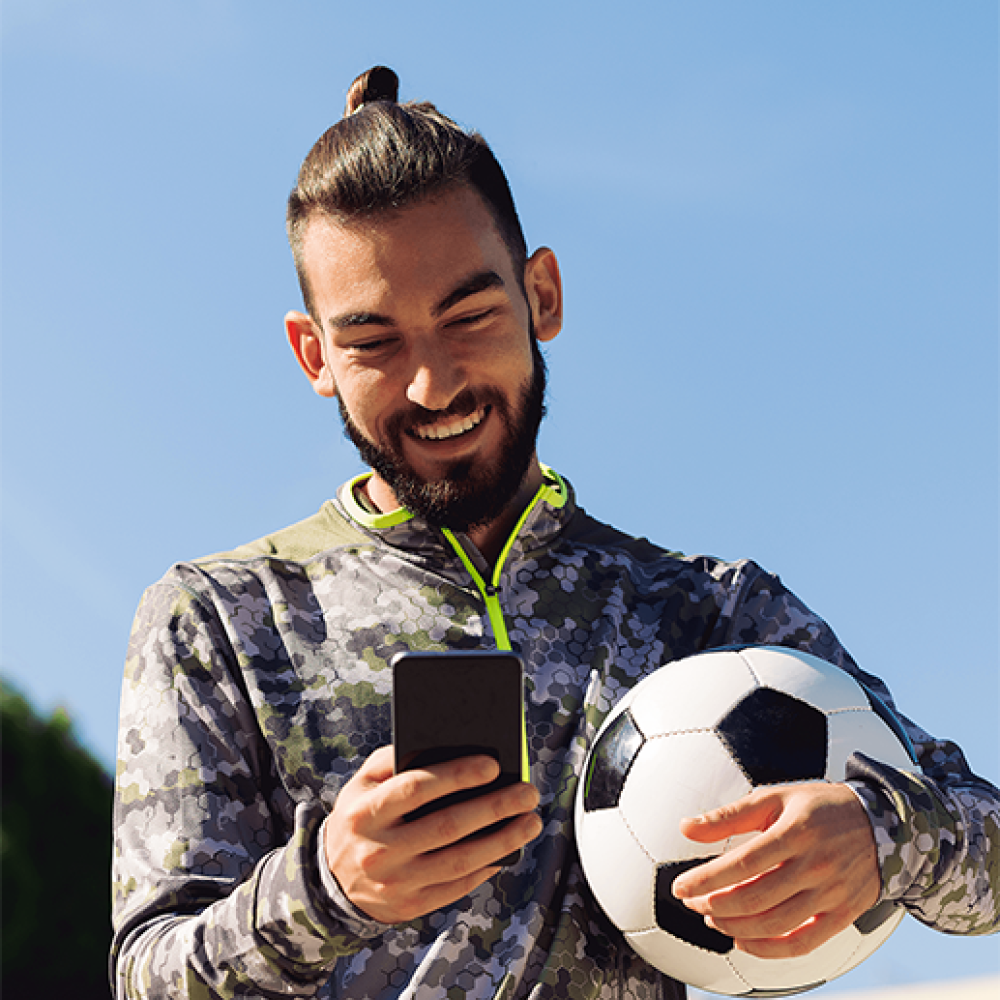 Young man holding a soccer ball and looking at his phone