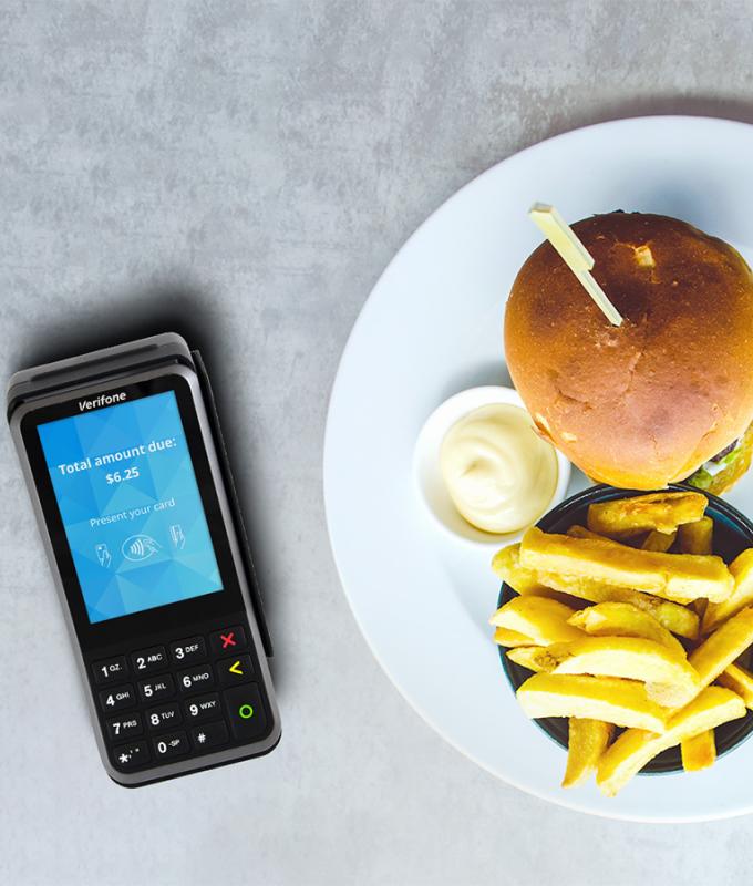 table with burger and fries on a plate beside the Verifone V400m payment device