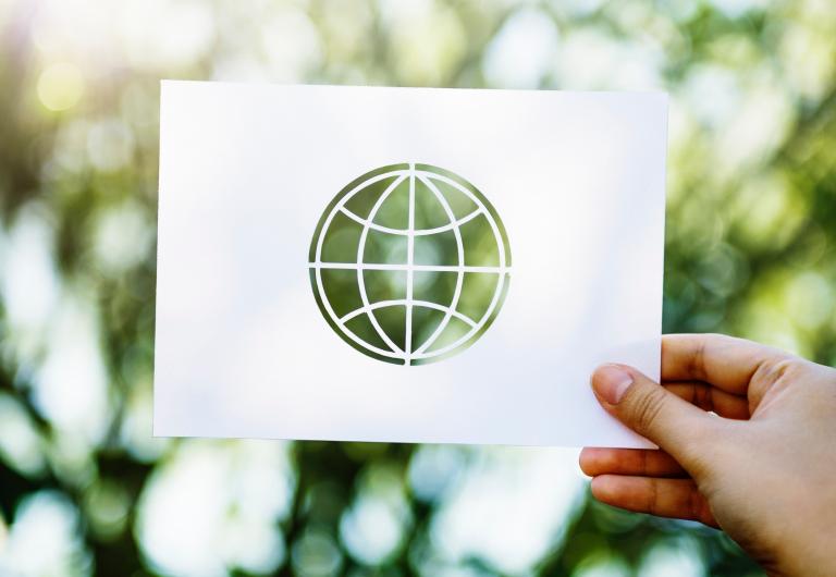 Hand holding up earth stencil in front of plants in the background