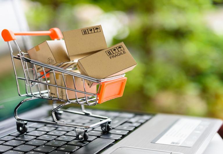 Miniature scale shopping cart with shipping boxes in it on top of a laptop keyboard